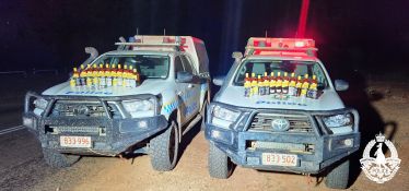 Two police vehicles with seized alcohol on bonnet.